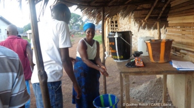 Liberia: A woman washes her hands at a CARE handwashing station before going shopping